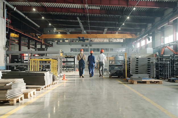 Foto retrovisor de três técnicos ou engenheiros da planta industrial em workwear saindo da oficina no final do expediente