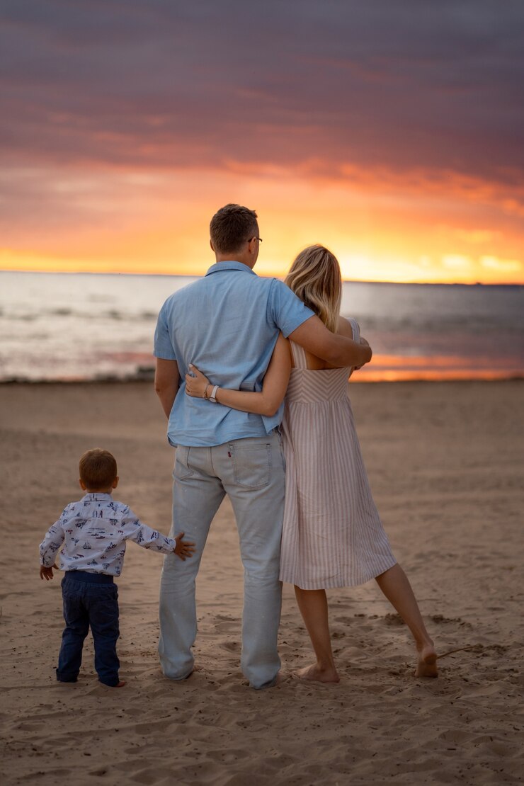 Foto retrovisor de um casal feliz se abraçando na praia no pôr do sol menino parado perto deles