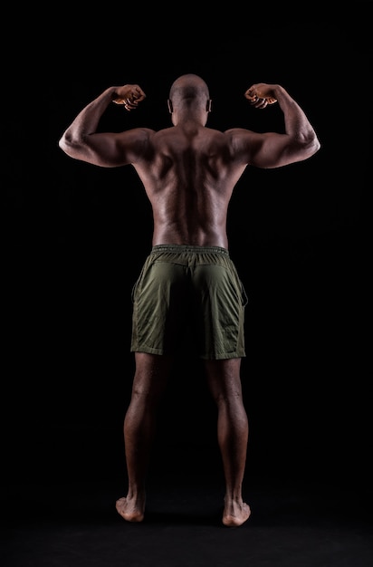 Retrovisor de um homem musculoso afro-americano flexionando os músculos do braço em um fundo preto
