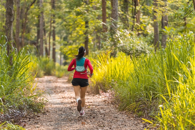 Retrovisor do corredor de trilha de mulher asiática adulta com colete de corrida pratica trilha correndo na floresta