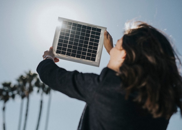 Retrovisor de mujer ecológica sosteniendo un panel solar en el cielo