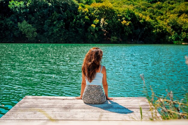 Retrovisor Uma bela jovem está sentada em um píer de madeira em um lago encantador de montanha azul