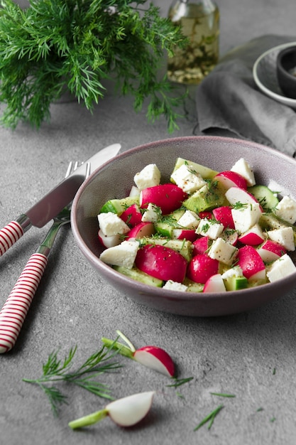 Rettich-, Gurken-, Kiwi-, Käse- und Dillsalat in einer Schüssel auf grauem Schmutzbetonhintergrund. Saisonale Küche, Food-Styling. Rohkostkonzept.