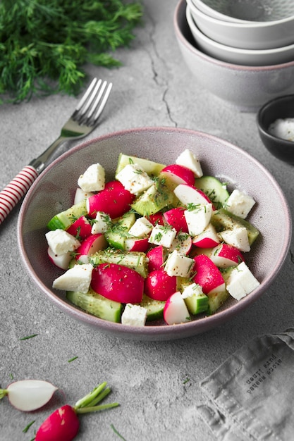 Rettich-, gurken-, kiwi-, käse- und dillsalat in einer schüssel auf grauem schmutzbetonhintergrund.