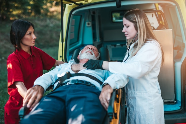 Rettungsdienst am Arbeitsplatz. Sanitäter zieht Bahre mit älterem Mann mit schwerem Herzinfarkt zum Krankenwagen. Unterwegs helfen. Fahrerassistenzkonzept.