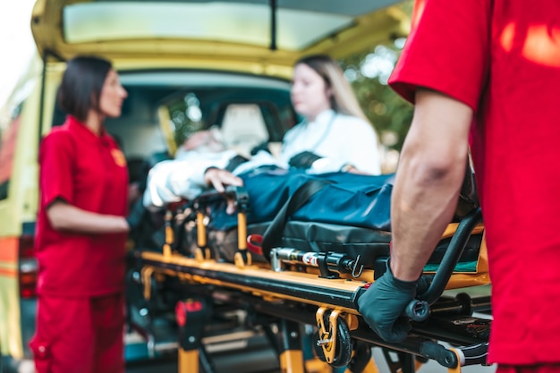 Foto rettungsdienst am arbeitsplatz. sanitäter zieht bahre mit älterem mann mit schwerem herzinfarkt zum krankenwagen. unterwegs helfen. fahrerassistenzkonzept.