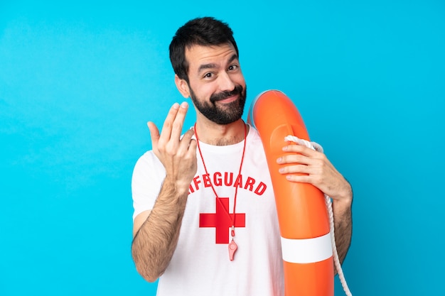 Rettungsschwimmer Mann über isolierte blaue Wand einladend, mit der Hand zu kommen. Schön, dass du gekommen bist