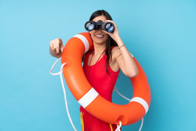 Rettungsschwimmerin über isolierter blauer Wand mit Rettungsschwimmerausrüstung und mit Fernglas