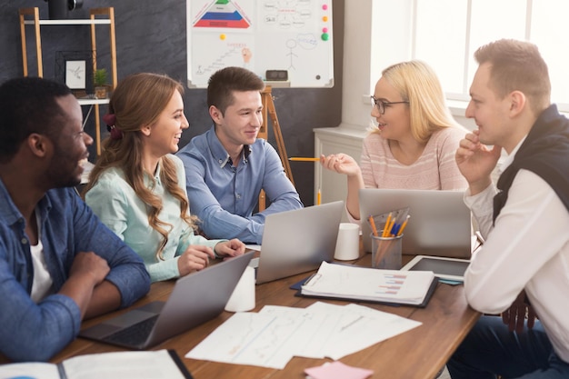 Reunião corporativa de negócios da equipe multiétnica. Jovens alegres fazendo um brainstorming, discutindo um novo projeto de inicialização no escritório, copiando o espaço