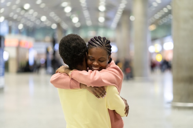 Reunião de família no aeroporto feliz negro abraçando uma mulher animada após a chegada do avião no terminal