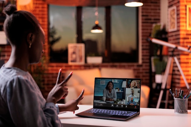 Reunião de negócios online com colegas de trabalho, brainstorming de equipe remota em teleconferência. Empresária afro-americana conversando com colegas em videoconferência usando laptop, vista traseira