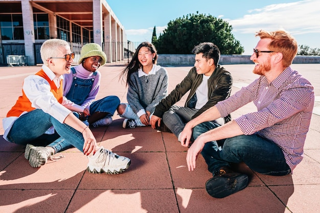 Reunión de amigos multiétnicos hablando y divirtiéndose sentados en el suelo