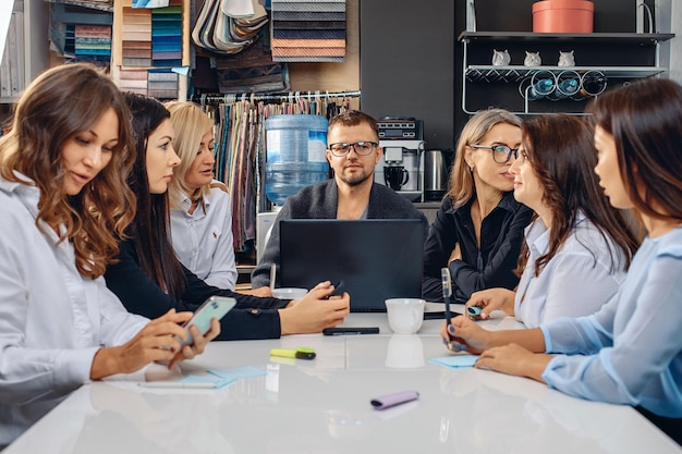 Reunión y discusión del proyecto. Jefe masculino joven y activo discutiendo un proyecto con sus colegas femeninas mientras está sentado en una mesa blanca en una oficina con un entorno creativo. Concepto de trabajo