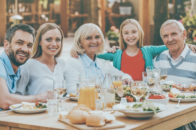 Reunión familiar. Familia feliz de cinco personas que se unen entre sí y sonríen mientras están sentados en la mesa de comedor al aire libre