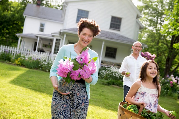 Una reunión familiar de verano en una granja, padres e hijos caminando por el césped llevando flores fr