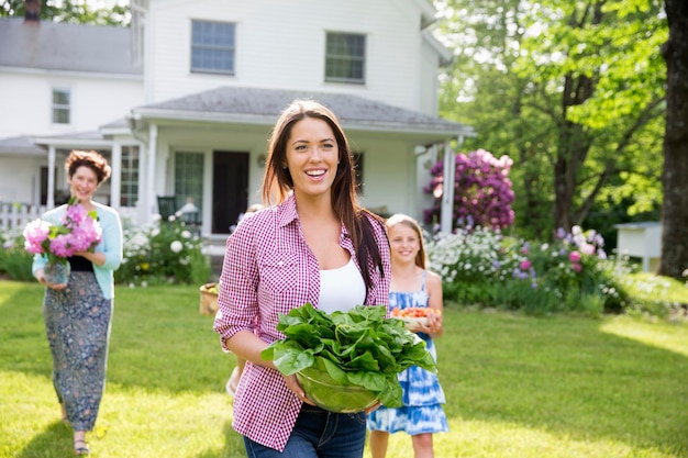 Una reunión familiar de verano en una granja, padres e hijos caminando por el césped llevando flores fr