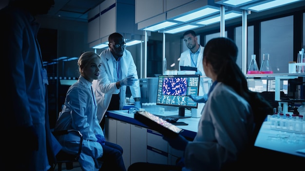 Reunión de laboratorios de investigación médica Diverso equipo de científicos utiliza computadoras tabletas digitales Discuten la biotecnología innovadora Laboratorio avanzado para el desarrollo de vacunas