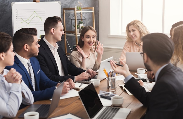 Reunión de negocios del equipo joven. Gente alegre intercambiando ideas, discutiendo la nueva estrategia de marketing en la oficina, espacio de copia