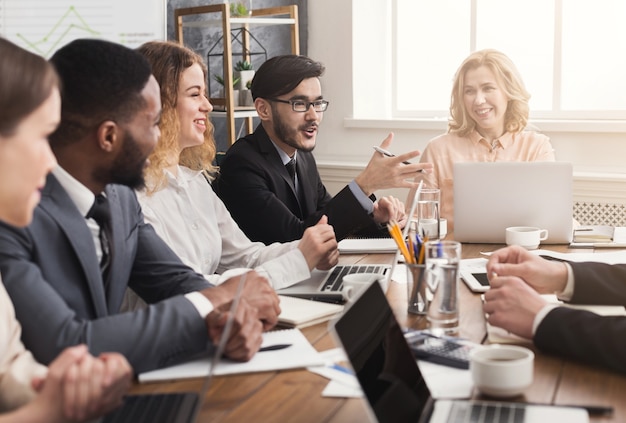 Reunión de negocios del equipo joven. Gente alegre intercambiando ideas, discutiendo la nueva estrategia de marketing en la oficina, espacio de copia