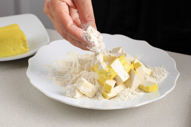 Revestimento à mão feminino fatiado de tofu amarelo com farinha, processo de cozimento para fazer tofu crocante (Tahu Krispi) na cozinha