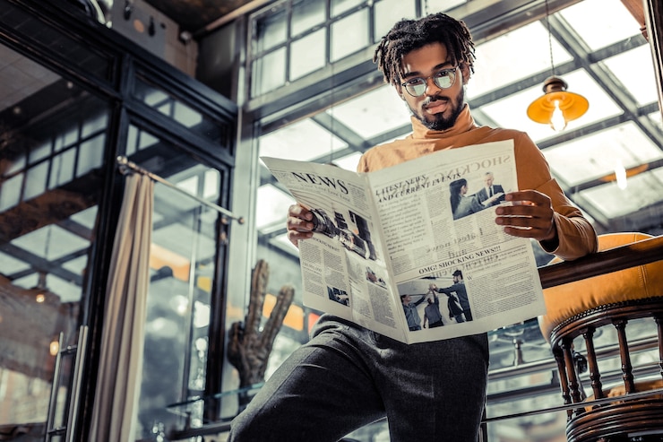 Foto revisão de notícias. homem internacional encantado usando óculos enquanto olha para o jornal