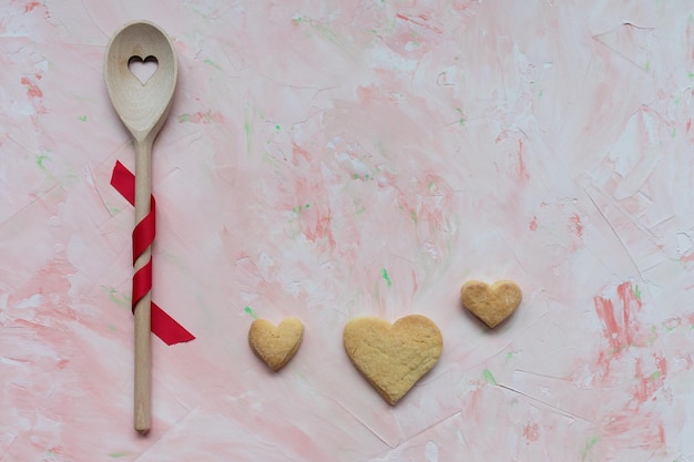 Revolviendo la cuchara y las galletas de mantequilla en forma de corazón sobre un fondo rosa