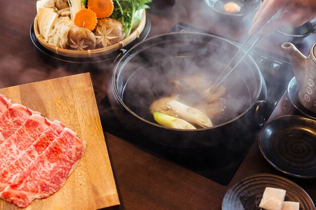 Foto revolviendo a mano el caldo shabu caliente e hirviendo con a5 wagyu y kurobuta de cerdo.