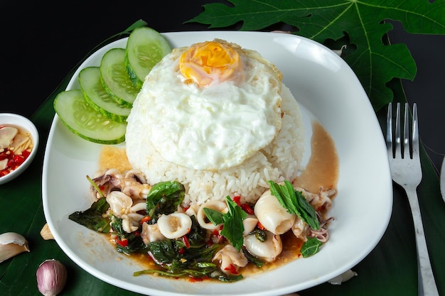 Revuelva la albahaca frita con calamares con arroz o mariscos arroz frito con albahaca comida tailandesa en mesa negra caliente y picante