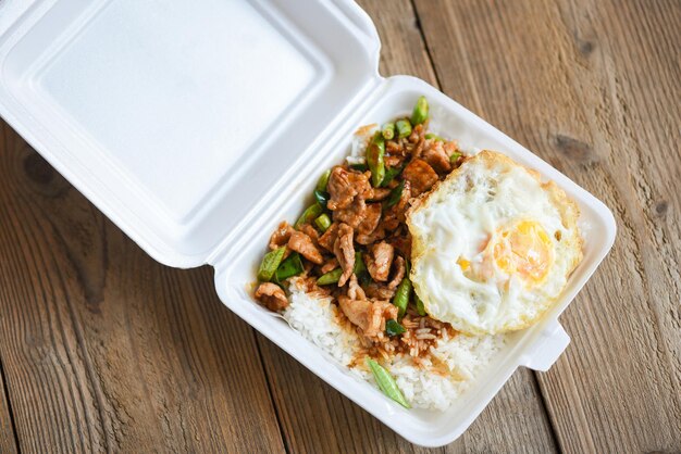 Revuelva el cerdo frito con pasta de curry rojo y hojas de albahaca con frijol largo y huevo frito cubierto en una caja de plástico Comida callejera tailandesa o entrega de alimentos