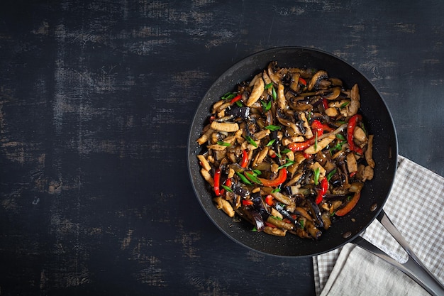 Revuelva freír con berenjena de pollo y pimienta en sartén wok sobre fondo oscuro