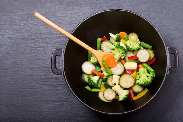 Revuelva las verduras fritas en un wok sobre fondo oscuro, vista superior