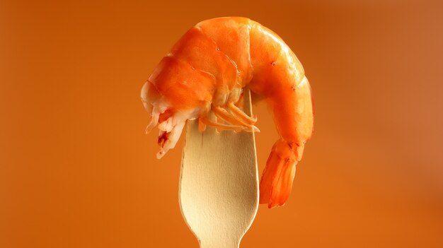 Un rey grande coció camarones en el fregadero en un tenedor de madera sobre un fondo marrón. Infraestructura de crustáceos del decápodo, comiendo carroña. Manjar del mar. Los camarones se utilizan para cocinar. Bocadillo de cerveza.