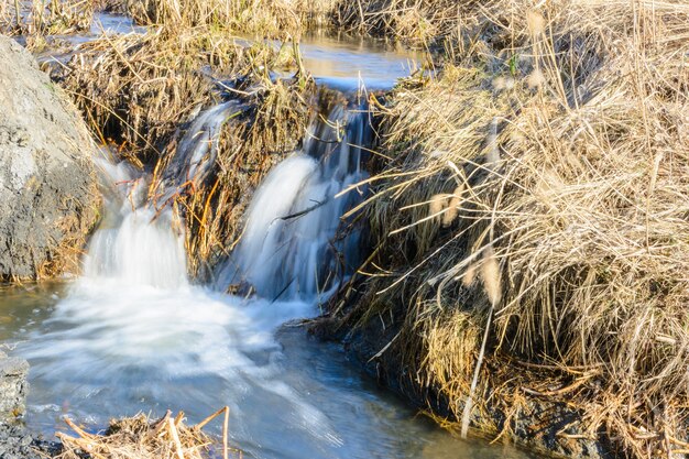 Riachos de primavera aguardados fluem sobre ravinas e colinas em um dia ensolarado. Corredeiras e cachoeiras de riachos entre o capim seco. Paisagem linda primavera.