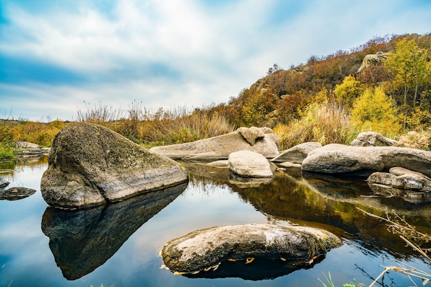 Un riachuelo rápido, poco profundo y limpio corre entre piedras grandes, lisas y húmedas rodeadas de grumos secos altos