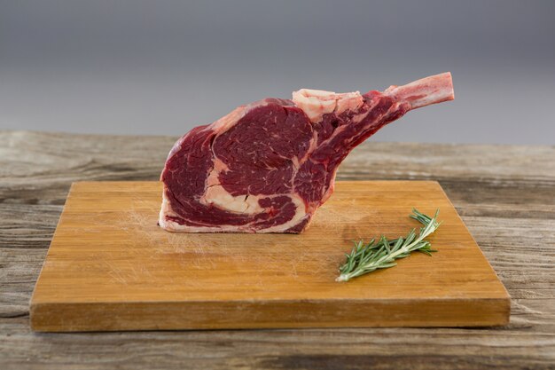 Rib Chop Steak und Rosmarinkraut auf Holzbrett gegen Holztisch