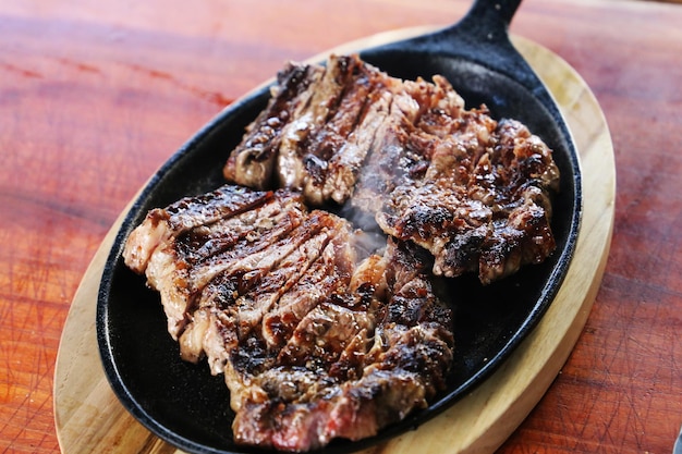 Foto rib eye piece of ancho steak cortado em uma panela de ferro sobre fundo de madeira