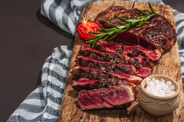 Ribeye-Steak auf seltenem Kochniveau mit Gewürzen und Kräutern, klassisches gegrilltes Fleisch, fertig zum Verzehr, Picknick- oder Abendessenkonzept, hartes Licht, dunkler Schatten, schwarzer Steinhintergrund, flach in Nahaufnahme liegend