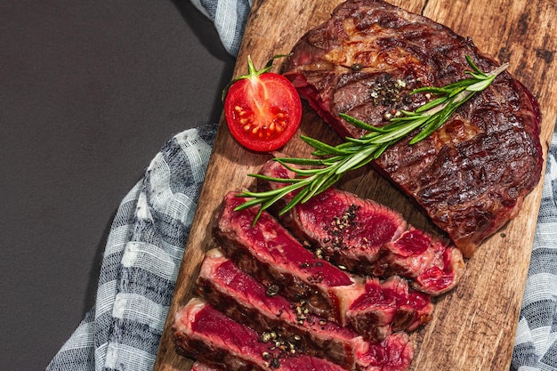 Ribeye-Steak auf seltenem Kochniveau mit Gewürzen und Kräutern, klassisches gegrilltes Fleisch, fertig zum Verzehr, Picknick- oder Abendessenkonzept, hartes Licht, dunkler Schatten, schwarzer Steinhintergrund, flache Lage von oben