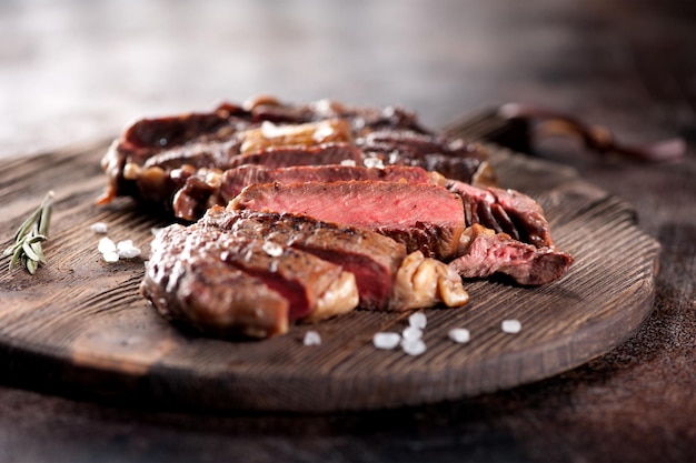 Ribeye-Steakscheiben mit Salz und Rosmarin auf einem Servierbrett aus Holz