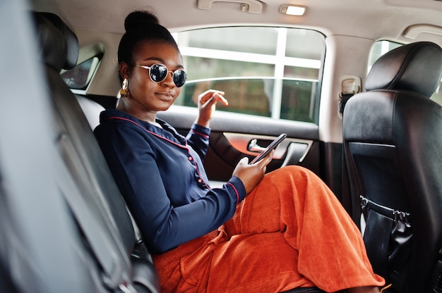 Rica mujer africana de negocios en gafas de sol sentarse en suv coche con asientos de cuero negro