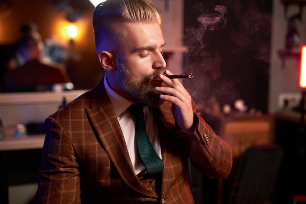Rico joven empresario en traje fuma un cigarro