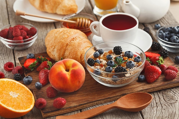 Rico y sabroso desayuno de fondo. Croissants con corteza dorada, muchas bayas orgánicas dulces y café sobre una tabla de madera sobre una superficie rústica. Delicioso comienzo del día.