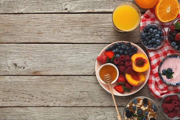 Rico y sabroso desayuno de fondo. Muesli, miel, vaso de jugo de naranja y tazón de frutas y bayas orgánicas dulces sobre una superficie rústica de madera, vista superior, espacio para copiar