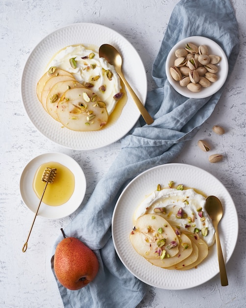 Ricotta con peras, pistachos y miel o jarabe de arce en la placa blanca.