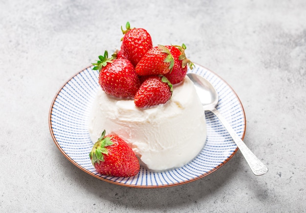 Ricotta de queso fresco italiano con fresas en un plato con una cuchara, fondo de piedra rústica gris