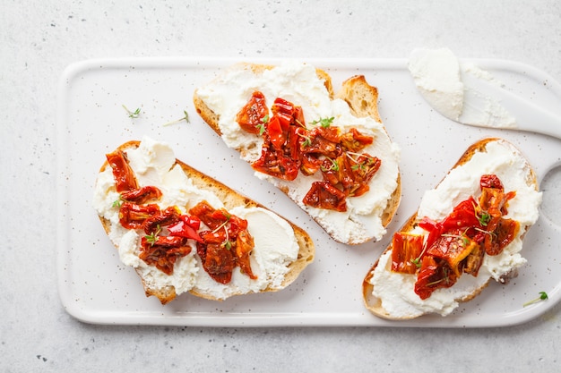 Ricotta und sonnengetrocknete Tomatensandwiche auf weißem Brett.