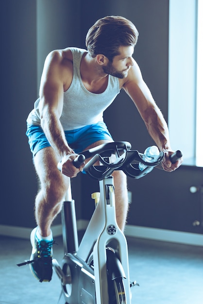 Ride para o sucesso. Jovem bonito em roupas esportivas, pedalando na academia