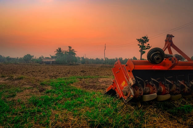 Ridging máquina de repressão. Fornecimento para trator. Máquinas agrícolas na fazenda agrícola. Exploração agrícola do arroz na manhã com o céu vermelho do nascer do sol. Natureza das terras agrícolas. Cabana do fazendeiro e pólo elétrico na terra.