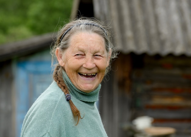 Riendo abuela anciana cerca de casa rural. Anciana rusa en el pueblo