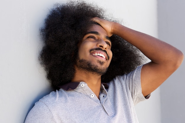 Riendo al hombre afro con la mano en el cabello mirando a otro lado